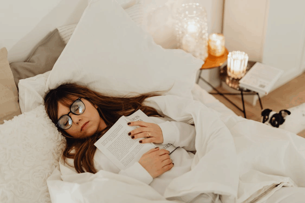 Woman falling asleep with a book in bed, practicing intuitive rest and letting her body slow down.
