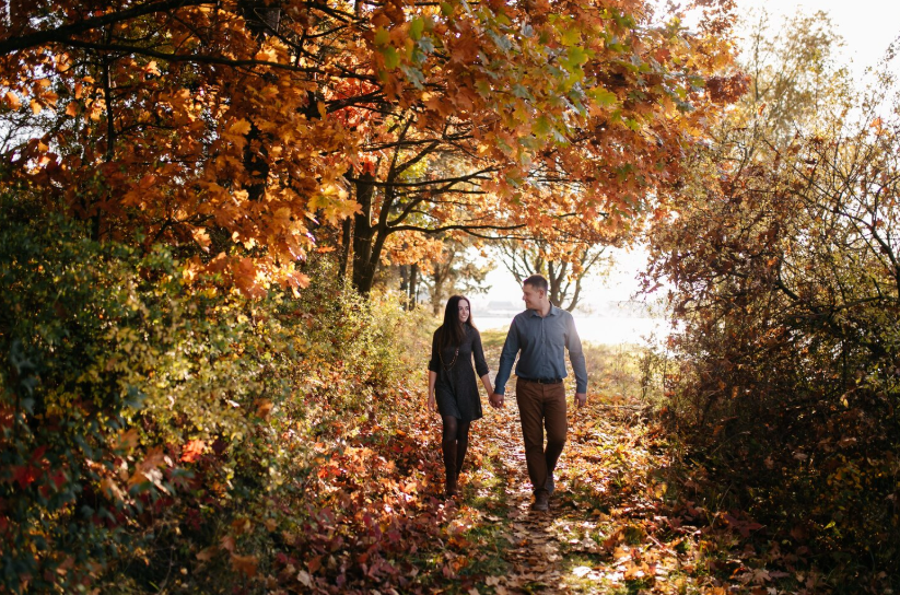 Couple walking through autumn forest path practicing seasonal living and connecting with nature.