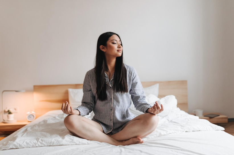 Woman in pajamas on her bed, practicing a calm morning meditation as part of simple daily ritual ideas.