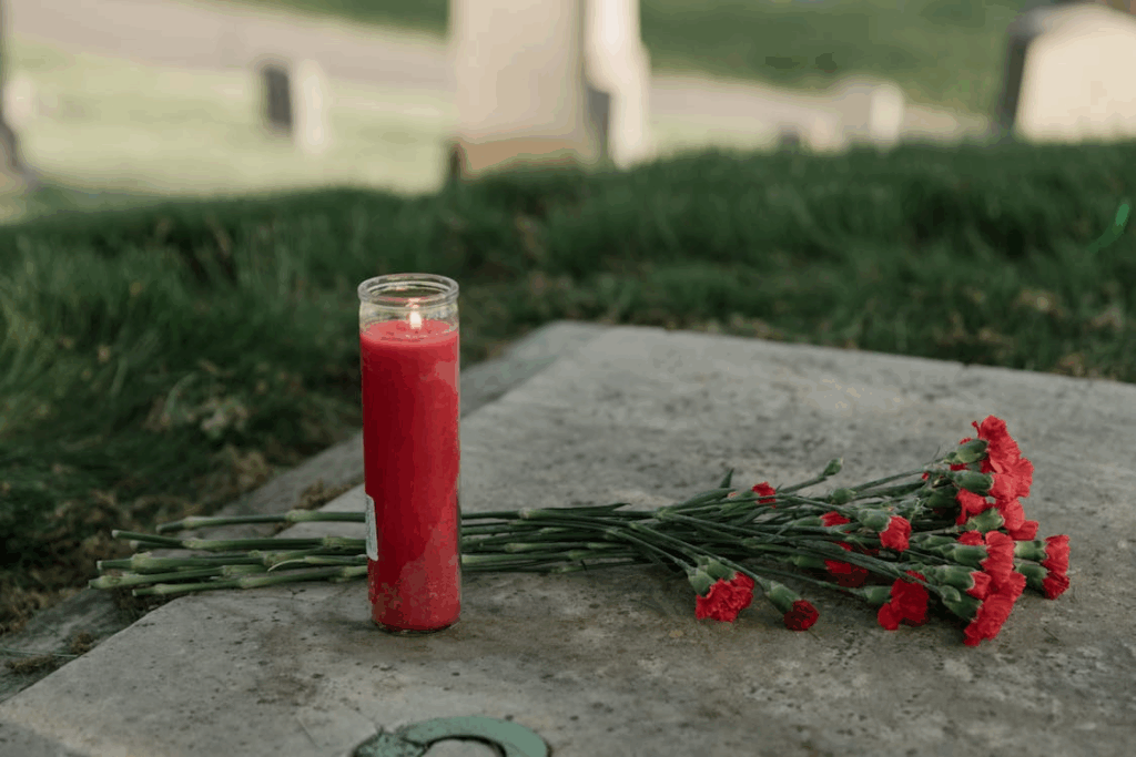 Red memorial candle and carnations placed on a grave to honor ancestors.