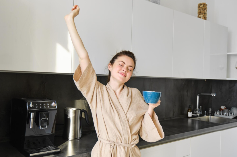 Woman in robe and enjoying morning coffee in kitchen as part of a simple five-item routine.