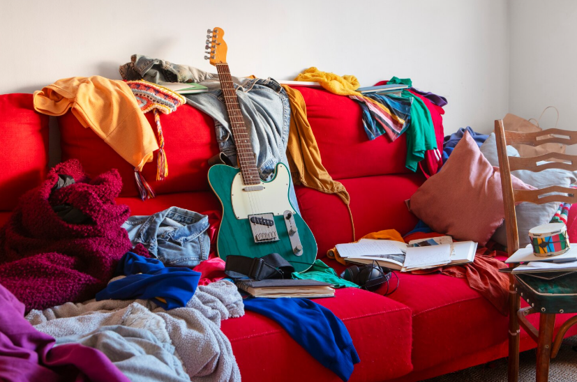 Messy sofa covered in clothes, guitar, books and blankets showing the emotional weight of home clutter.