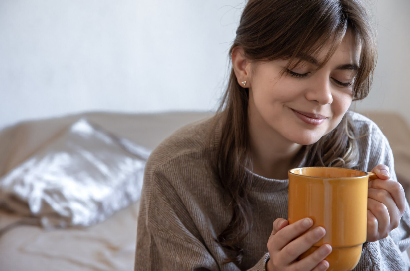 Woman savoring a warm drink, eyes closed, enjoying the calming benefits of slowing down.
