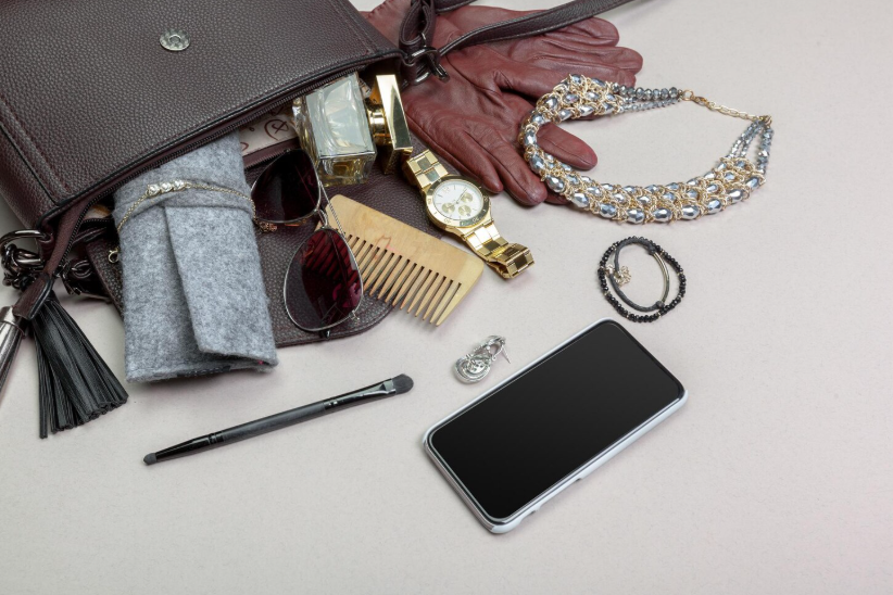 Flatlay of capsule accessories including handbag, watch, jewelry, sunglasses, gloves, and phone arranged neatly.