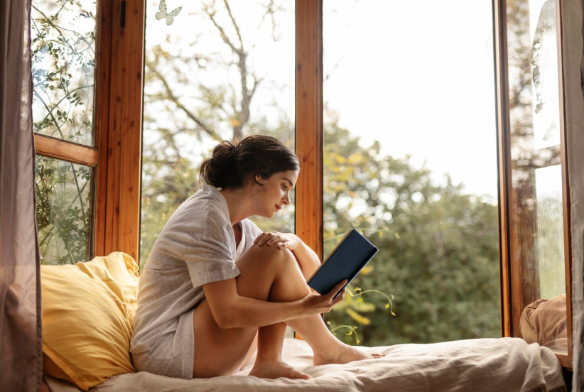 Woman reading in a cozy window nook at home, enjoying a quiet mini-retreat for reflection.