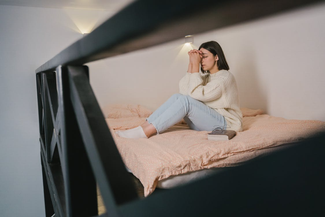 Woman sitting on bed with eyes closed and hands together, taking ten minutes of silence for calm and reflection.