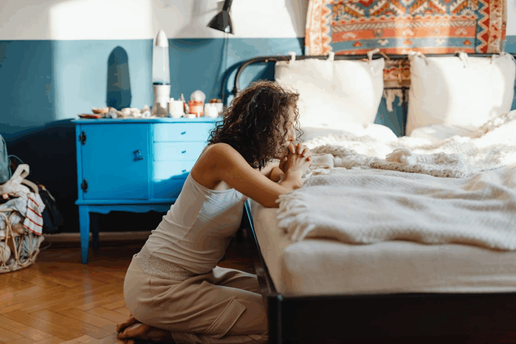 Woman kneeling beside her bed, praying quietly and creating an everyday spirituality moment.