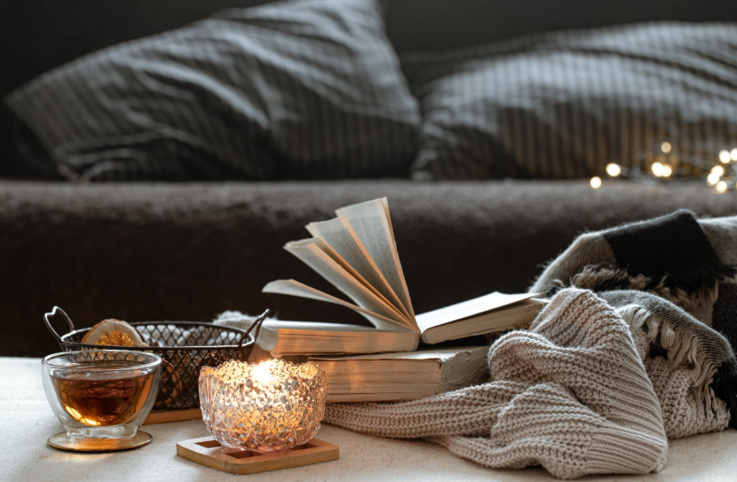 Warm evening wind-down scene with open book, lit candle, cup of tea, and soft blanket.